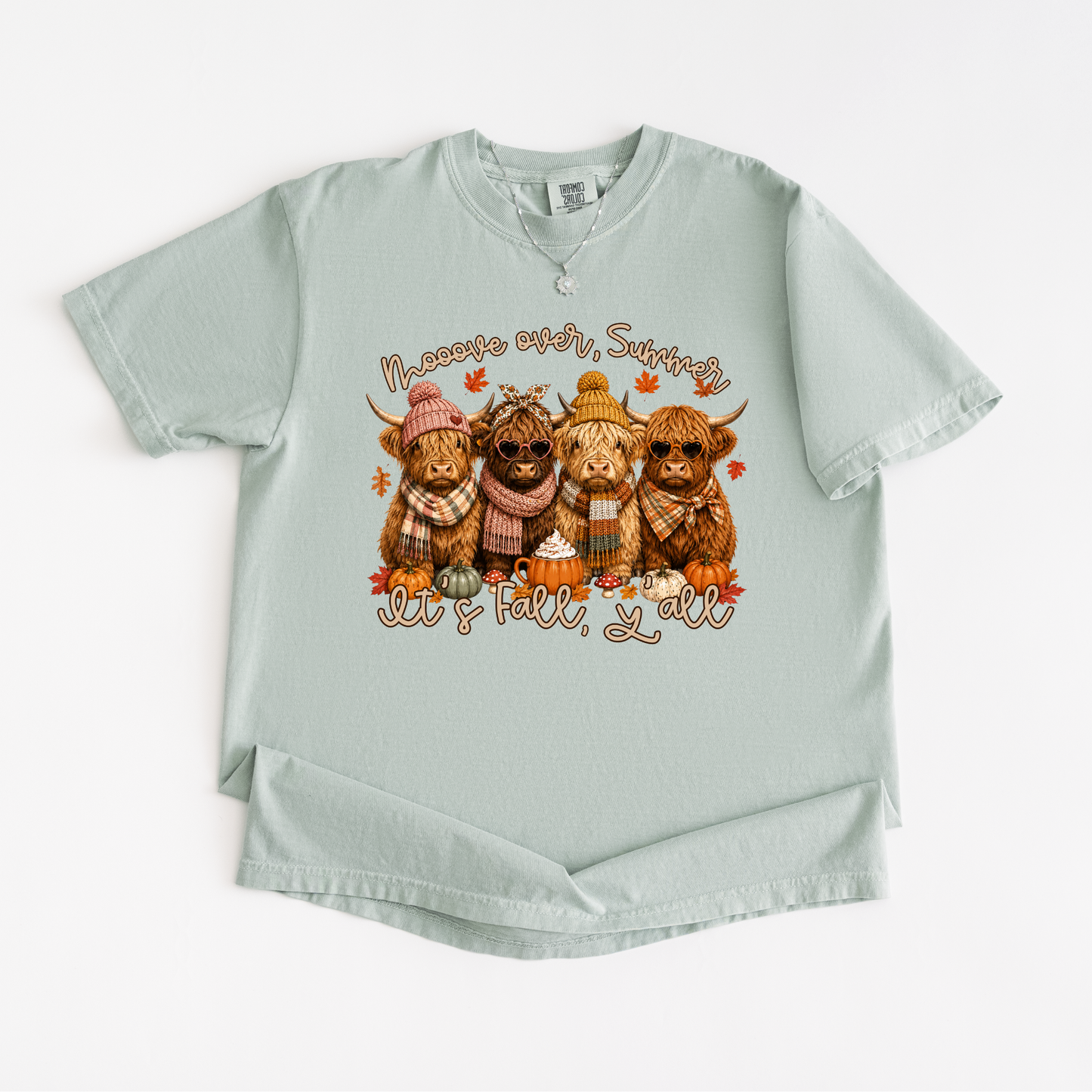 A light sage green short-sleeve t-shirt with a graphic of four Highlanders wearing autumn clothing and pumpkins, with the text 'Halloween over, Saturday' and 'Get 'tall, y'all' printed on the front.