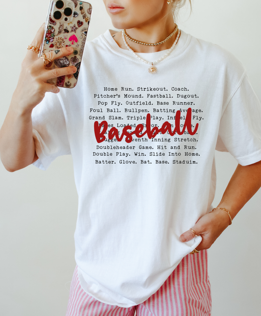 Person wearing a white t-shirt with baseball-related text, holding a phone with a colorful case.