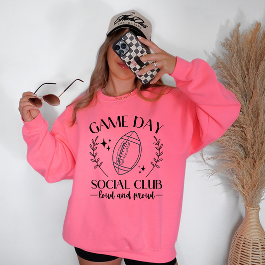 Person wearing a pink sweatshirt with 'Game Day Social Club' text and a football graphic, holding sunglasses and a phone.