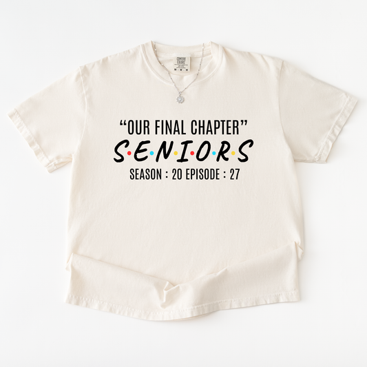 An off-white short-sleeve t-shirt with a graphic print on the front. The print features the text '“OUR FINAL CHAPTER” SENIORS SEASON : 20 EPISODE : 27' styled like the iconic Friends TV show logo, with the word 'SENIORS' in black and the letter accents in red, yellow, and blue.