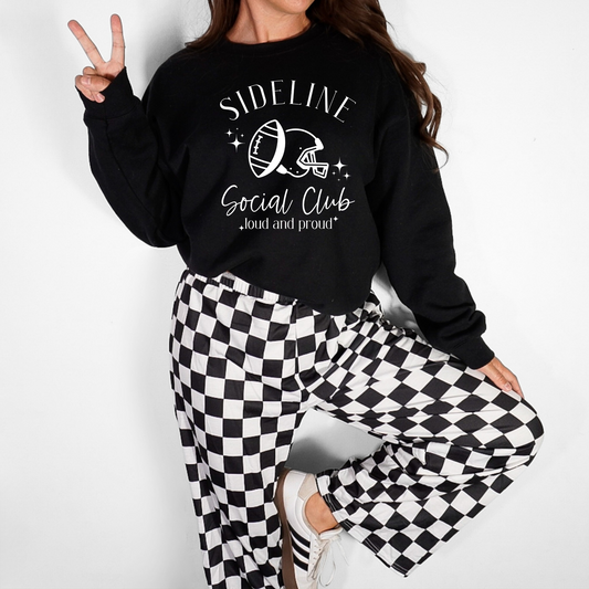 Person wearing a black sweatshirt with 'Sideline Social Club' text and checkered pants on a white background