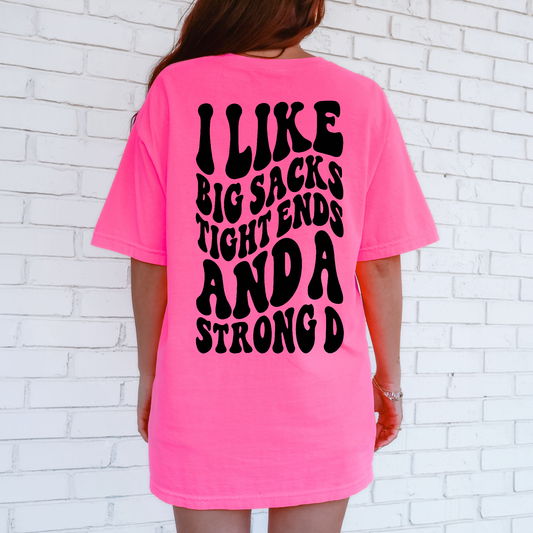Person wearing a bright pink t-shirt with black text against a white brick wall.